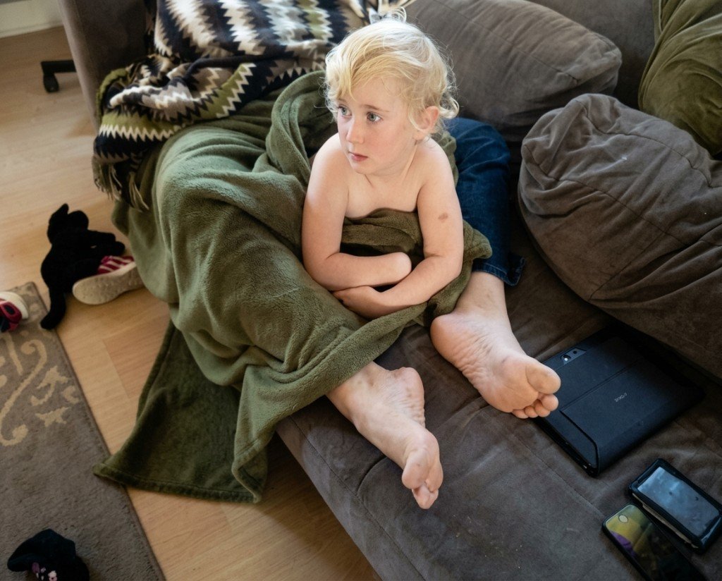 Enfant assis sur un canapé, les pieds d'un adulte créent l'illusion de pieds géants
