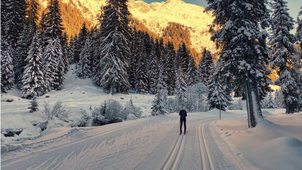 Skieur de fond sur une piste enneigée face aux sommets au soleil levant